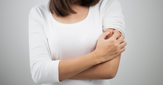 A woman in a white shirt scratching her arm, symbolizing the challenges of "All About Rosacea, Eczema, Redness, & Sensitive Skin."